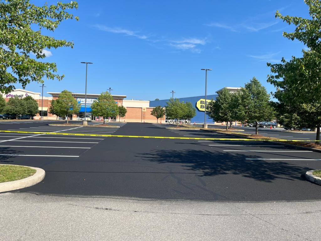 A recently sealed and striped parking lot is roped off with caution tape.